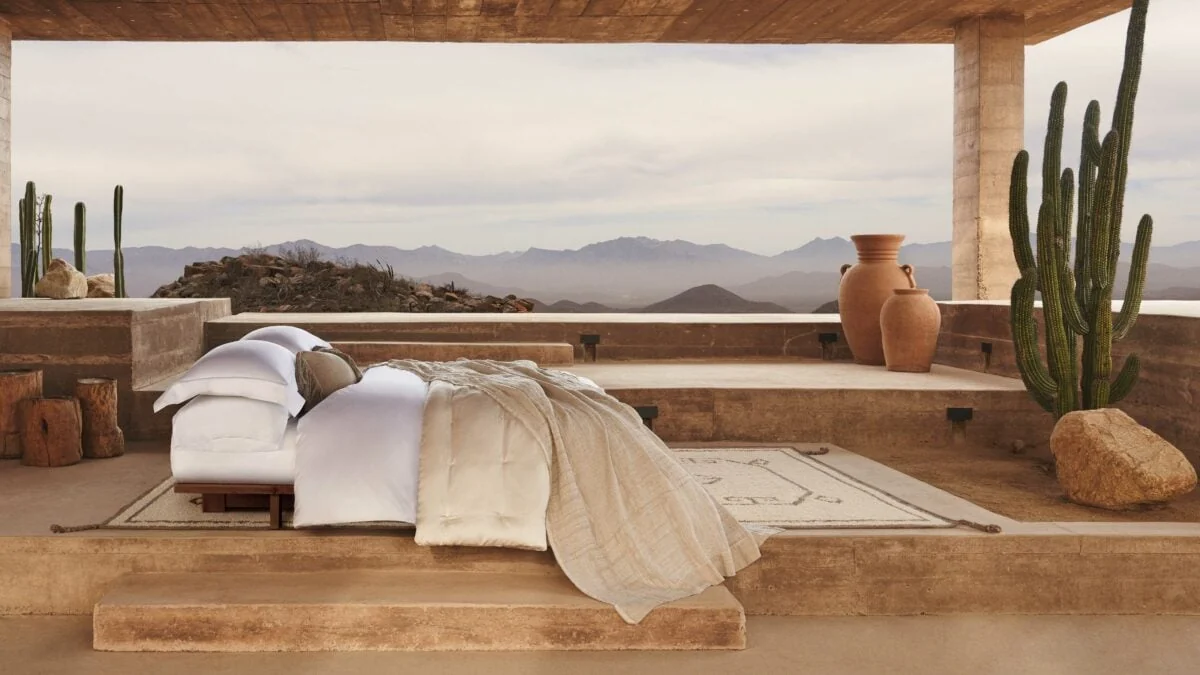 White bedding on a bed set on an open adobe terrace with saguaro cacti, clay urns and desert mountains, for Banana Republic.