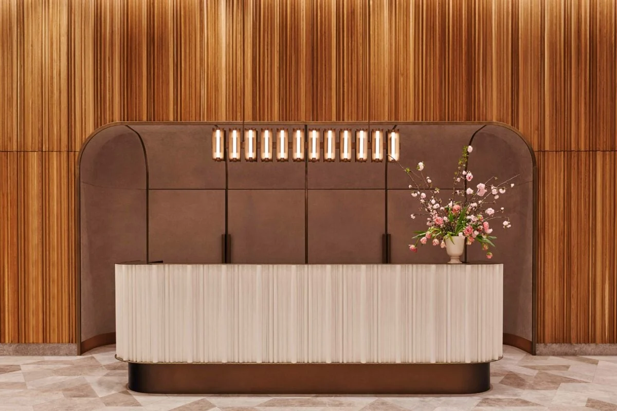 Lobby reception desk with fluted cream front, wood-slat walls, pendant lights and pink blossoms, for Brooklyn Tower.