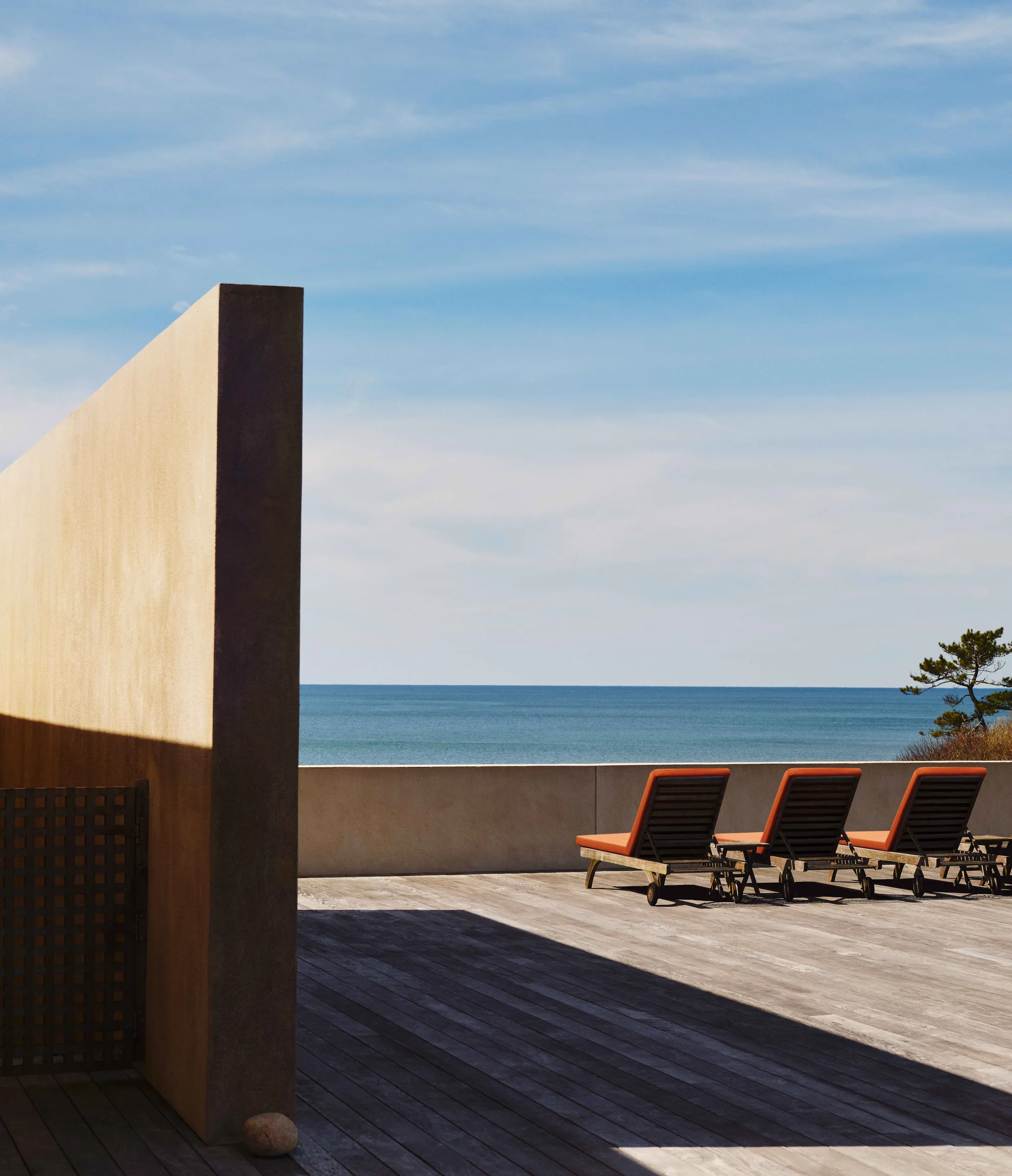 Wooden deck with three orange-cushioned loungers beside a concrete wall overlooking the ocean, for Wall Street Journal.