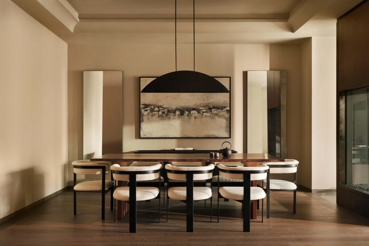Dining room with cream chairs, wooden table, black dome pendant and abstract painting in warm light, for Aman.