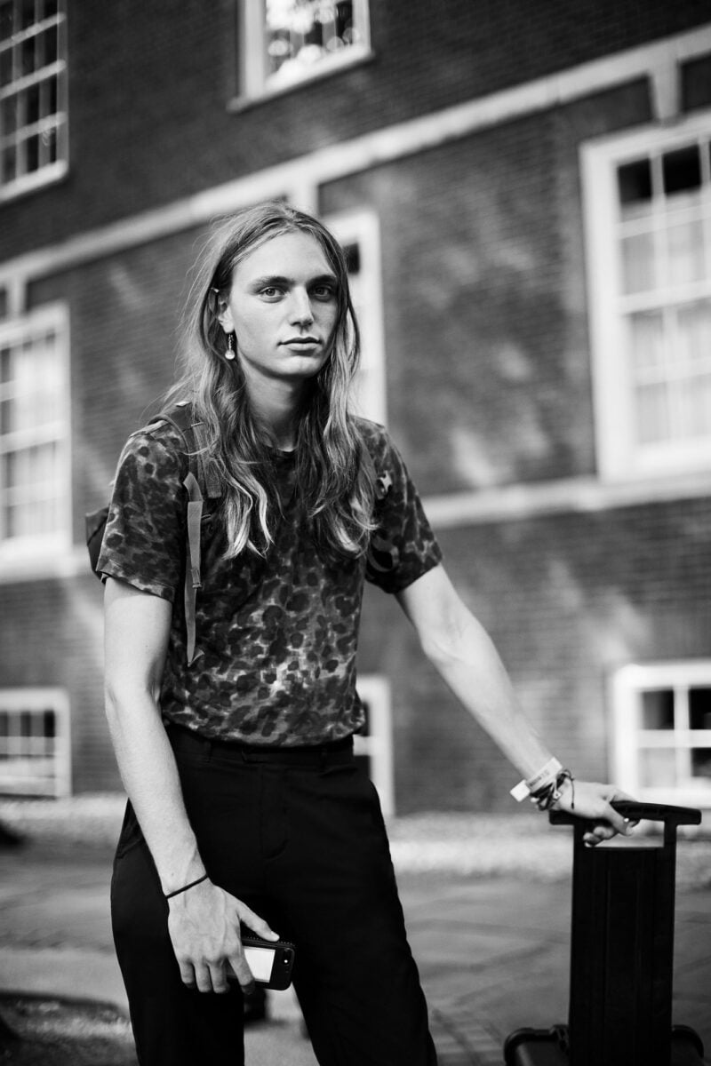 Black-and-white street portrait of a long-haired model in a leopard tee holding a suitcase handle, for The Sartorialist.